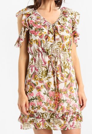 Femme portant une robe sans manches à imprimé floral avec un col à volants, une ceinture à la taille et un ourlet volanté dans des tons roses, jaunes et verts.