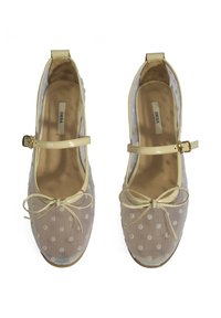 Transparente Ballettschuhe mit Polka-Punkten, einem cremefarbenen Lackriemen und einer Schleifendetail. Flache Sohle mit einem beige Innenfutter und sichtbarem Markenlabel.