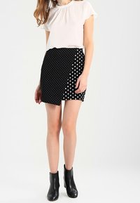 Černá sukně s puntíky a asymetrickým střihem, doplněná bílou blůzkou s krátkým rukávem. Černé kotníkové boty celý outfit dotvářejí.