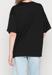 Czarny, oversize t-shirt wykonany z materiału bawełnianego, z okrągłym dekoltem i krótkimi rękawami. Prosty design bez widocznych wzorów czy akcentów.