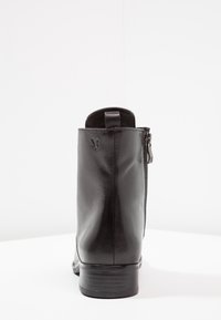 Bottine en cuir noir à finition lisse, avec une fermeture éclair latérale et un talon bas empilé. Dotée d'une languette à l'arrière pour un enfilage facile.