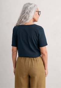 Dark teal short-sleeved top with a rounded neckline, paired with light brown, gathered wide-leg pants, both in smooth fabric.