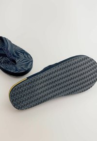 Flip-flop blu navy con un motivo a foglia sulla parte superiore e una suola di gomma texture con design a zigzag e accenti gialli sul bordo.