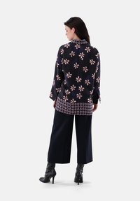 Long-sleeved blouse in navy with floral pattern, featuring a round collar and a contrasting geometric hem. Paired with wide-leg black pants and heeled boots.