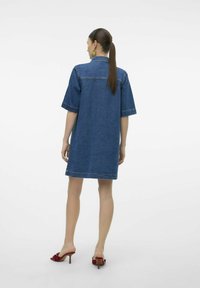 Denim skjortekjole med korte ermer og kragehals, med en løs passform og mørkeblå farge. Brukt med røde hælhæler.