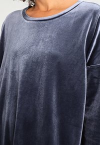 Sammetströja i mörk marinblå, med rund halsringning och lös passform, samt mjuk textur och långa ärmar.