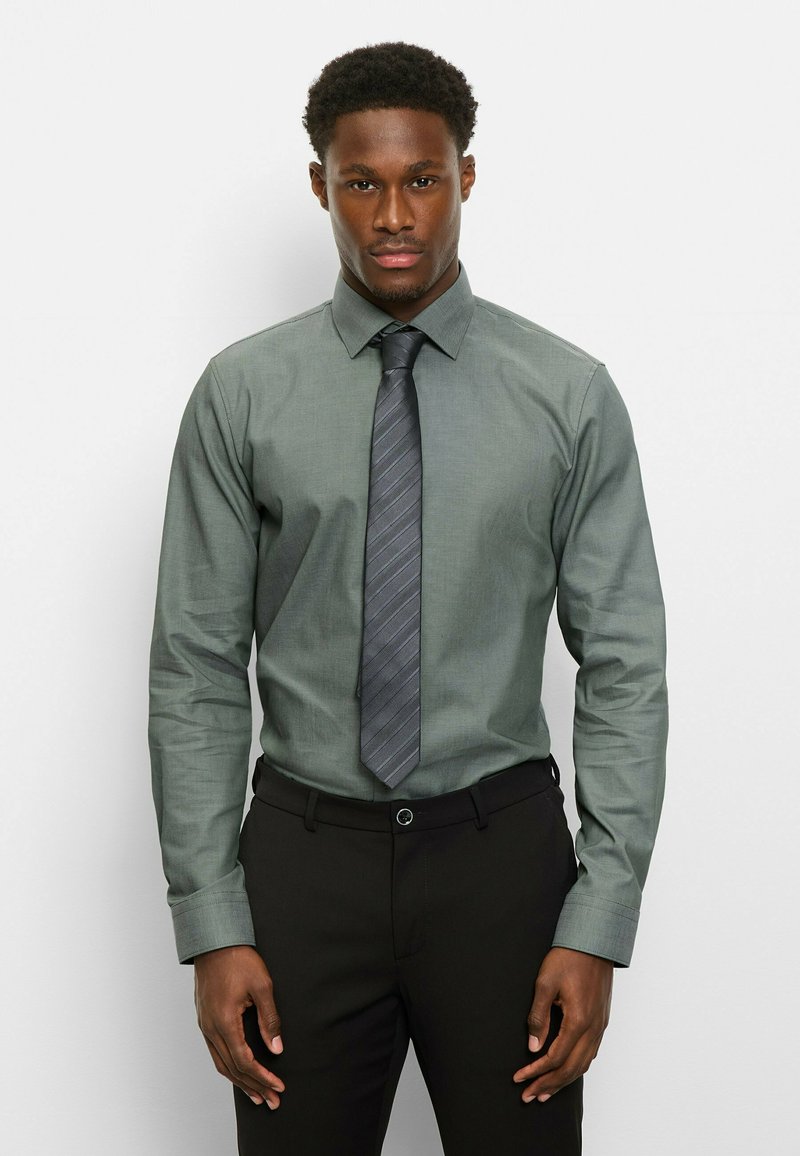 Grünes Langarmhemd mit einem strukturierten Kragen, kombiniert mit einer grau gestreiften Krawatte. Das Hemd hat eine glatte Textur und ein schlankes Design.