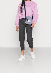 Ljust lila sweatshirt, mörkgrå jeans och vita sneakers. Liten blå väska med "TOMMY"-logotyp på axelremmen. Enkelt, avslappnat outfit.