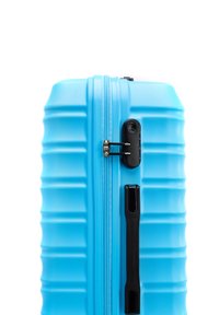 Valise rigide bleue avec texture rainurée, fermeture éclair centrale et accents noirs, y compris un mécanisme de verrouillage et une poignée latérale.