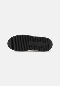 Semelle de basket en caoutchouc noir avec des rainures horizontales et un logo en relief. Le design présente une pointe arrondie et un motif texturé pour une meilleure adhérence.