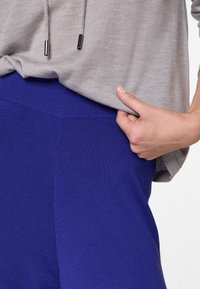 Grijze pullover met metalen koorddetails, gecombineerd met koninklijkblauwe stof, met een geribde tailleband en een gladde textuur.