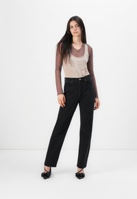 Black high-waisted jeans with a straight-leg fit, paired with a beige layered tank top and long-sleeve shirt. Black pointed shoes with bows.
