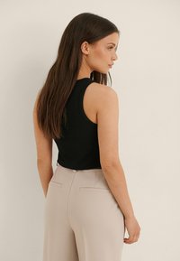 Črna rebrasta majica s tankimi naramnicami in oprijetim krojem, kombinirana s svetlobeznimi hlačami visokega pasu z zadnjimi žepi in gladko teksturo.