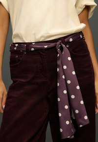 Fialové manžestrové nohavice s textúrovaným povrchom, s pásom so svetlofialovými bodkami previazaným v páse a neformálnym bieločiapovým topom.