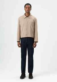 Beige cropped jasje met een kraag, gecombineerd met donkerblauwe spijkerbroek en bruine schoenen. Eenvoudig ontwerp, gladde textuur.