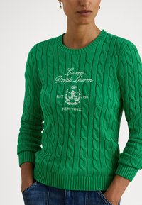 Camisola verde de malha com padrão em trança, decote redondo, punhos e bainha canelados, com logótipo bordado no peito em branco.