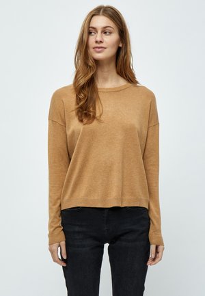 Maglione lungo color marrone chiaro con scollatura e polsini a costine. Vestibilità casual, morbido al tatto, indossato con pantaloni neri.