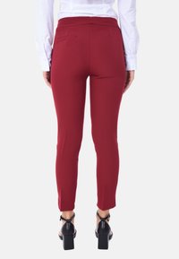 Pantaloni aderenti rossi con una texture liscia, vita media e tasche posteriori. Indossati con una camicia bianca e scarpe nere con tacco quadrato.