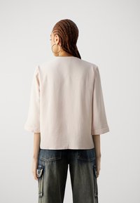 Top strutturato di un rosa chiaro con scollo rotondo e maniche a tre quarti, abbinato a pantaloni cargo in denim blu dal taglio morbido.