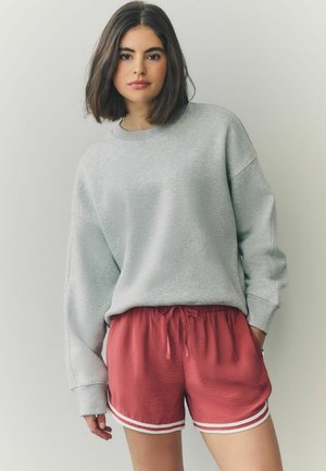 Grijze fleece sweatshirt met verlaagde schouders, gecombineerd met rode shorts met een trekkoord en witte zijkanten. Glad textuur.