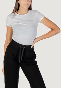 Witte t-shirt met korte mouwen en een zilveren logo, gecombineerd met zwarte sweatpants met zijzakken en een trekkoord in de taille. Nette stofstructuur.