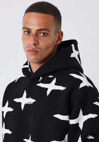 Felpa nera con un evidente motivo a stelle bianche, realizzata in tessuto morbido, dotata di un logo frontale e un cappuccio con coulisse.