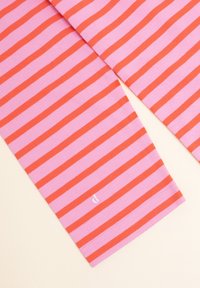 Rosa T-Shirt mit horizontalen roten Streifen, aus weichem Baumwollmaterial. Verfügt über ein kleines weißes Logo-Detail am Saum. Einfaches, lässiges Design.