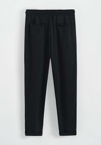 Pantalons de survêtement noirs en tissu doux, avec une taille élastique, deux poches avant et une conception de jambe fuselée avec des ourlets côtelés.