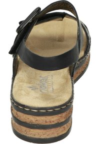 Svart lädersandal med korkplattform, justerbar rem och mjuk beige fotbädd. Nästa sömdekoration längs kanten av sulan.