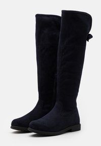 Bottes bleu marine montant jusqu'au genou, en faux daim doux, avec une fermeture éclair latérale et un nœud décoratif en haut. Semelle plate en caoutchouc.
