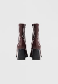 Bottines en cuir bordeaux avec un design ajusté, fermeture éclair et un talon cranté imposant. Texture lisse avec des détails de couture en contraste.