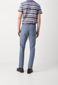 Hellblaue Baumwollhose mit glatter Textur, figurbetontem Schnitt und zwei Gesäßtaschen. Kombiniert mit einem gestreiften blauen und beigen Oberteil.