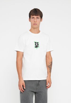 Witte katoenen t-shirt met een zwart en groen grafisch logo op de borst, gecombineerd met grijze spijkerbroek. Soepele textuur, relaxte pasvorm.