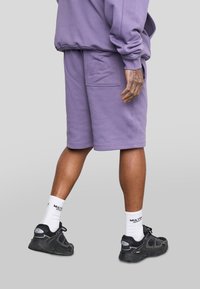 Paarse shorts gemaakt van zachte stof, met zijzakken en ribgebreide zoom. Gecombineerd met zwarte sportschoenen en witte crew sokken.