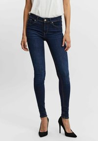 Jean skinny en denim bleu foncé à taille haute, avec une fermeture éclair, cinq poches et des détails de couture subtils.