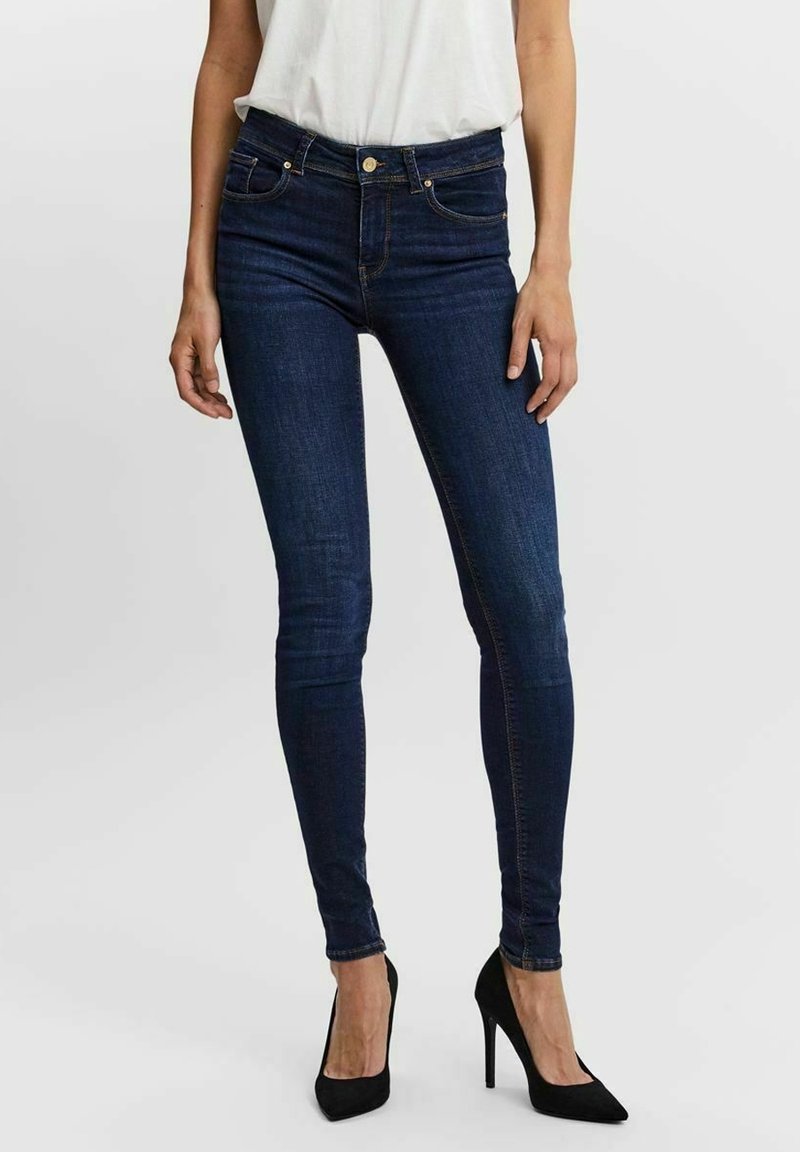 Jean skinny en denim bleu foncé à taille haute, avec une fermeture éclair, cinq poches et des détails de couture subtils.