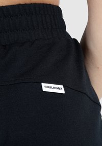 Black sports shorts with a ribbed waistband and a white "SMILODOX" label on the lower side. Fabric appears soft and slightly textured.