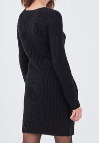 Robe noire tricotée avec une texture côtelée, manches longues et encolure ronde, mettant en valeur une silhouette ajustée jusqu'au mi-thigh.