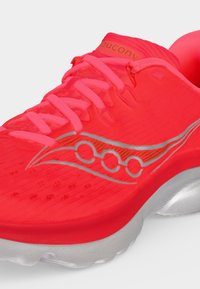 Φωτεινό κόκκινο αθλητικό παπούτσι Saucony με ροζ κορδόνια, ασημένιο λογότυπο στο πλάι και λευκή σόλα με επενδυμένο τμήμα στη φτέρνα.