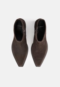 Paire de bottines en daim brun foncé avec bouts pointus et fermetures éclair latérales, vues de dessus sur fond blanc.