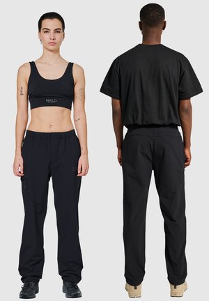 Schwarzes Activewear-Set mit einem enganliegenden Sport-BH mit "HALO"-Logo und locker sitzenden Hosen mit seitlichen Reißverschlüssen. Beide aus glattem, leichtem Material gefertigt.