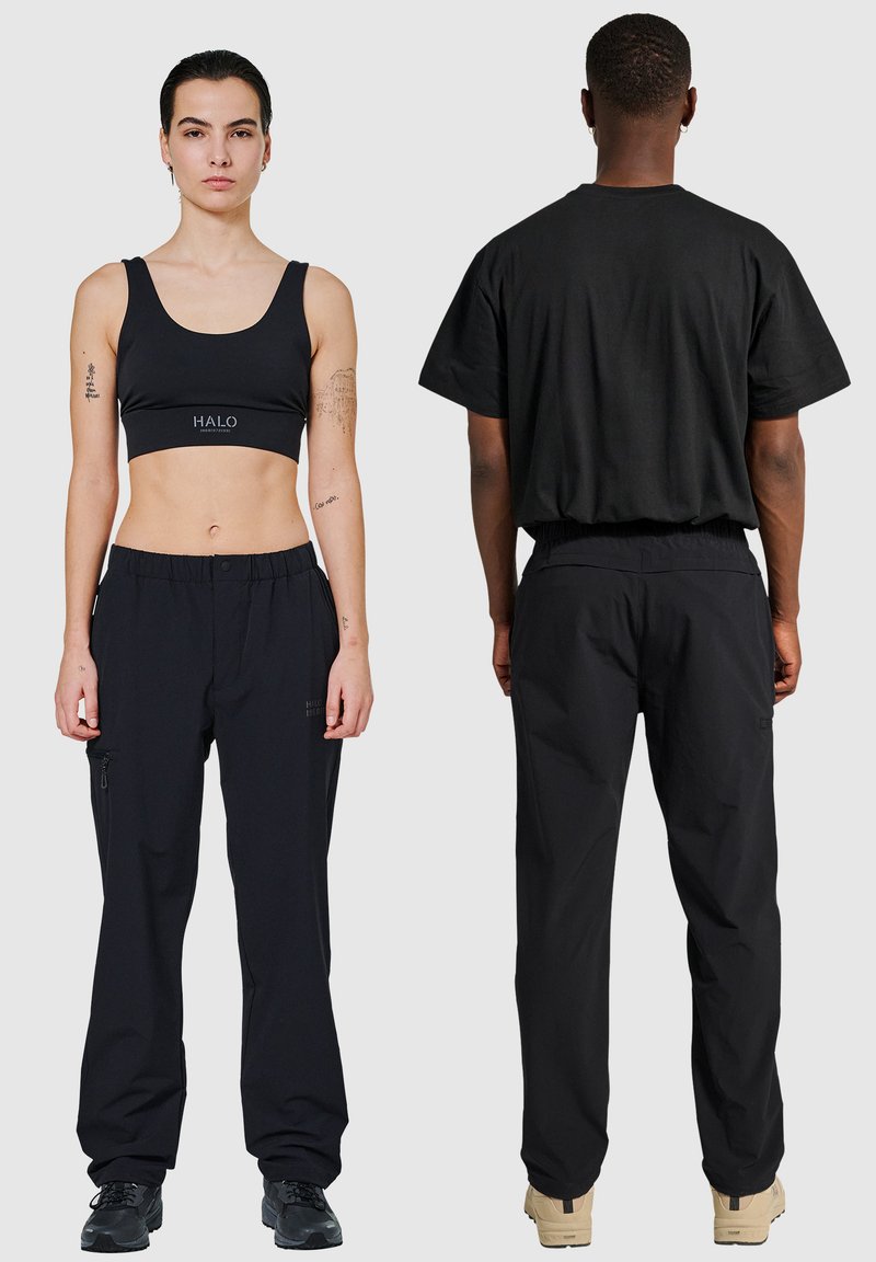 Schwarzes Activewear-Set mit einem enganliegenden Sport-BH mit "HALO"-Logo und locker sitzenden Hosen mit seitlichen Reißverschlüssen. Beide aus glattem, leichtem Material gefertigt.