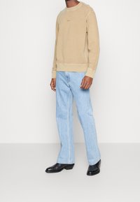 Beige sweat-shirt med rund hals och subtil logga, kombinerad med ljusblå, löst sittande jeans och svarta ankelstövlar. Enkelt design och mjukt material.