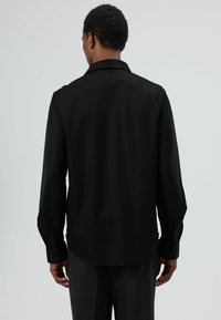 Chemise noire à manches longues avec une texture lisse, col classique, poignets boutonnés et un ourlet légèrement incurvé, confectionnée dans une coupe ajustée.