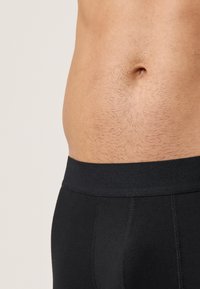 Schwarze, eng anliegende Boxer-Shorts mit einem glatten, elastischen Bund. Der Stoff ist weich und dehnbar und liegt eng an der Haut an.