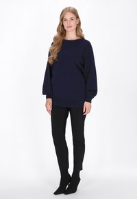 Granatowy, oversize'owy sweter z długimi, obszernymi rękawami i ściągaczami na mankietach, w połączeniu z czarnymi spodniami slim fit i czarnymi botkami za kostkę.