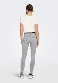 Ανοιχτό γκρι στενά τζιν με ψηλή μέση, δύο πίσω τσέπες και διακριτική ξεθώριαση, συνδυασμένα με ένα απλό λευκό t-shirt και αθλητικά παπούτσια.