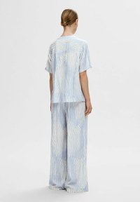 Camicetta a maniche corte a righe blu e bianche abbinata a pantaloni palazzo coordinati. Il tessuto ha una consistenza morbida e un design fluido.