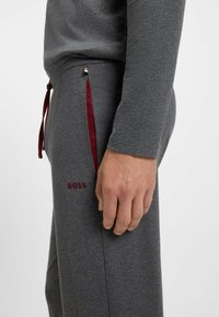 Harmaat verkkarit, joissa on slim fit -leikkaus, maroonit nyörit, sivutaskut ja brodeerattu "BOSS" -logo reisissä. Pehmeä rakenne.