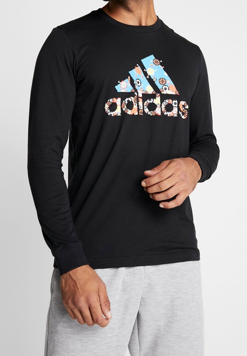 Schwarzes Langarmshirt mit mehrfarbigem Blumenmuster-Logo auf der Vorderseite, enganliegend, aus Baumwolle, kombiniert mit grauen Jogginghosen.